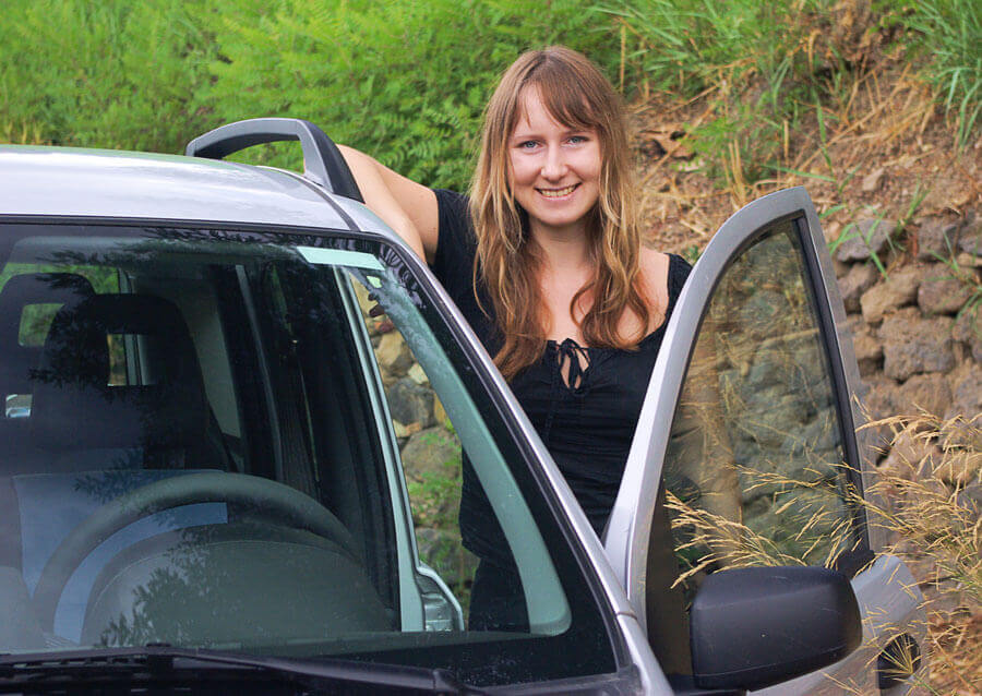 image of woman standing in driver side door and silver minivan with a smile