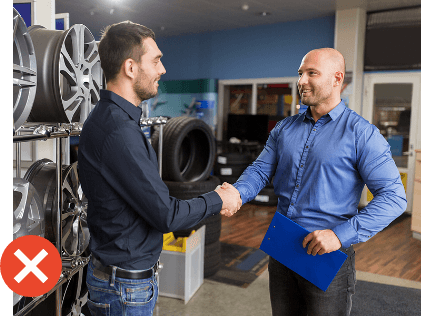 Generic Stock Image of two men in business shirts shaking hands in a tire shop with rims in background with a red 'x' on image