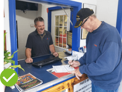 Owner of Hemlock Auto & Alignments in Hemlock MI with a customer signing paper at the front desk in auto repair shop with a green checkmark on image